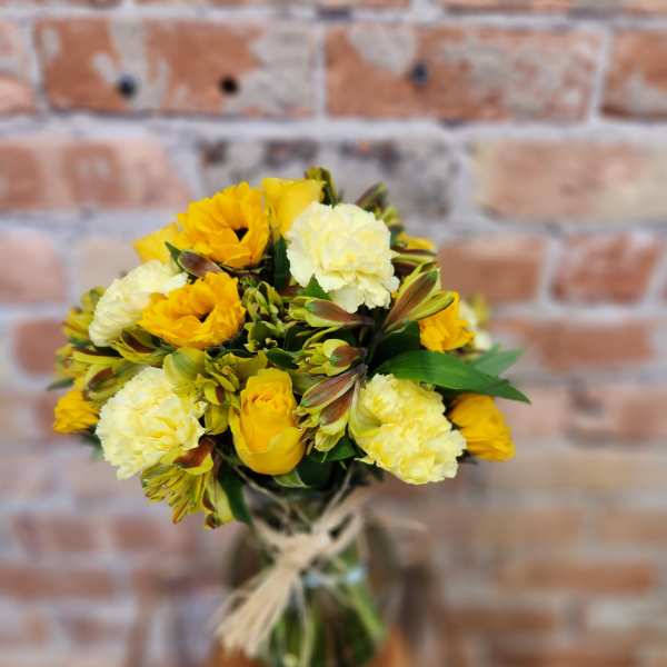 Yellow and cream bouquet in a glass vase with a twine tie