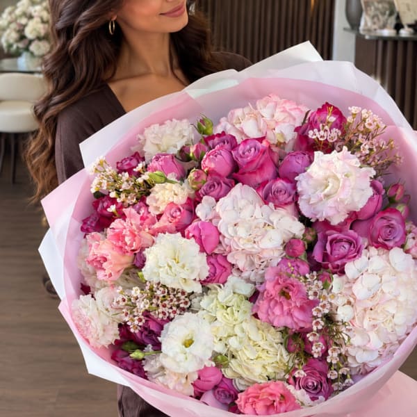Woman holding a large pink and white bouquet of roses and carnations