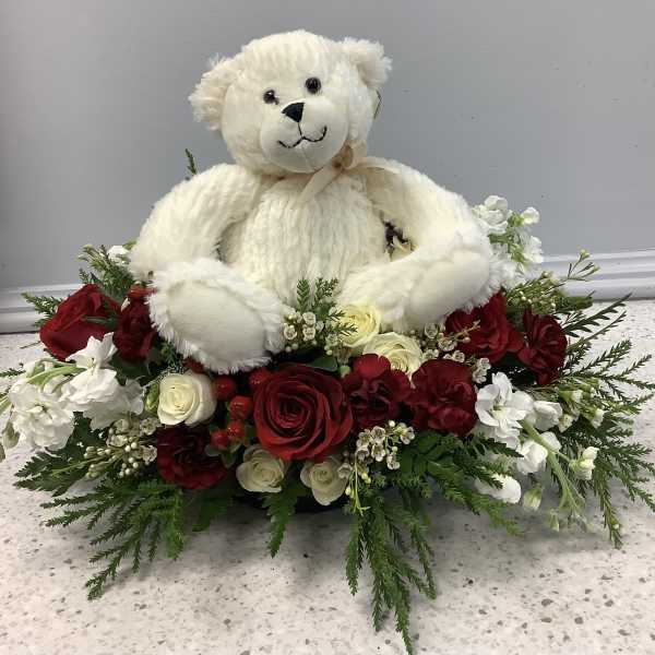 White teddy bear sitting in a red and white rose arrangement