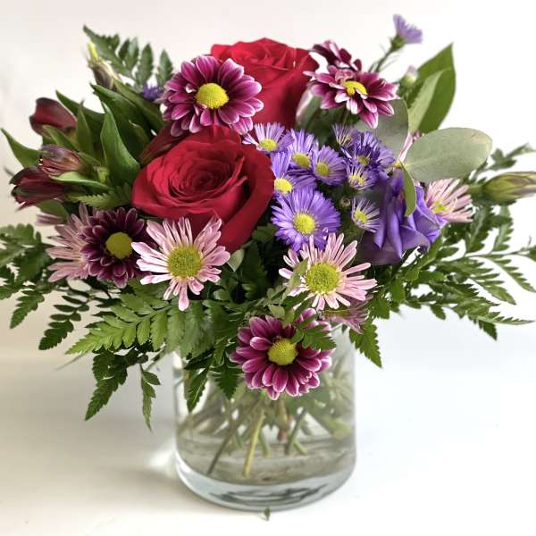 Bouquet of red roses and purple daisies in a glass vase