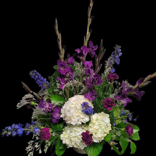 Purple and blue flowers arranged with white hydrangeas in a vase