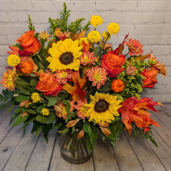 Autumn bouquet with sunflowers, orange roses, and yellow mums in a glass vase