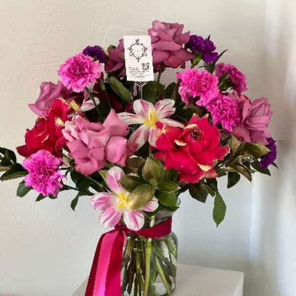 Pink and red mixed flower bouquet in a glass vase with a ribbon