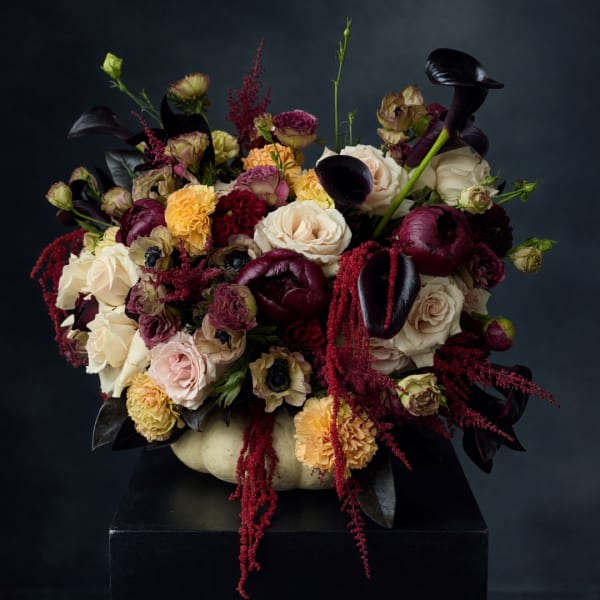 Dark floral arrangement in a pale pumpkin-shaped vase with roses and calla lilies