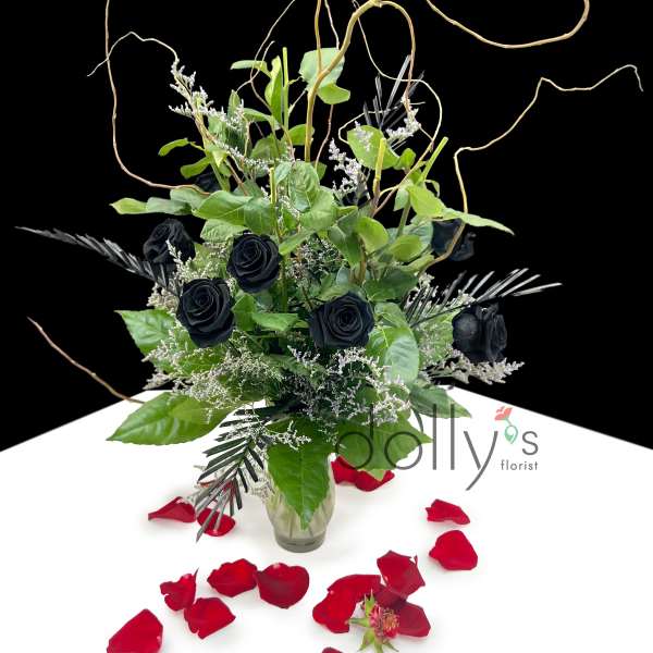 Black roses in a glass vase with red rose petals around it