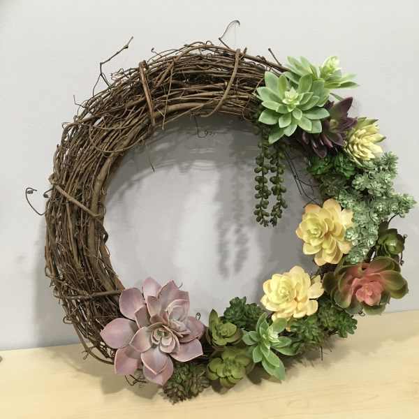 Succulent wreath on a grapevine ring with pink, yellow, and green rosettes