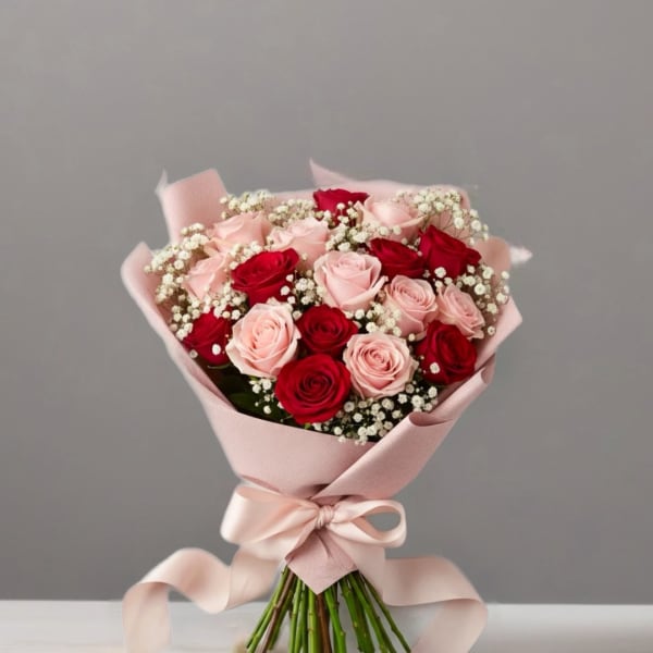 Bouquet of pink and red roses wrapped in pale pink paper with a ribbon