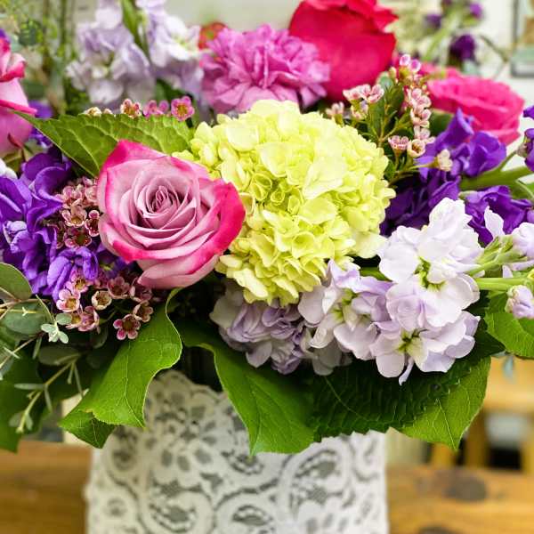 Mixed bouquet of pink, purple, and white flowers in a lace-wrapped vase