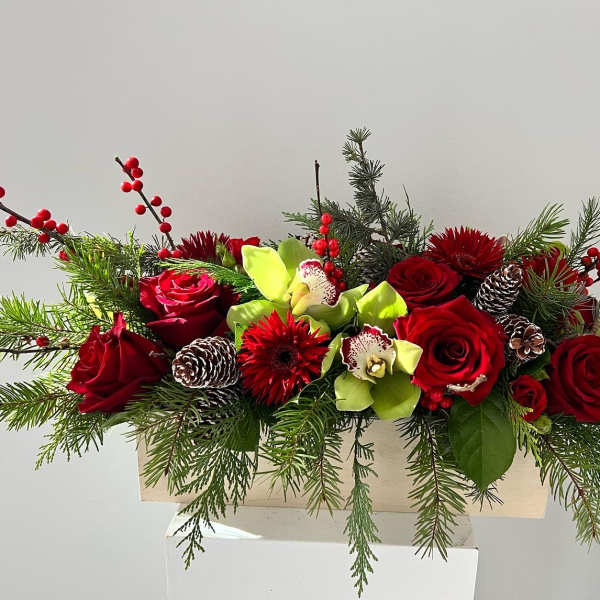 Red roses and green orchids arranged with pinecones and evergreen branches in a wooden box.