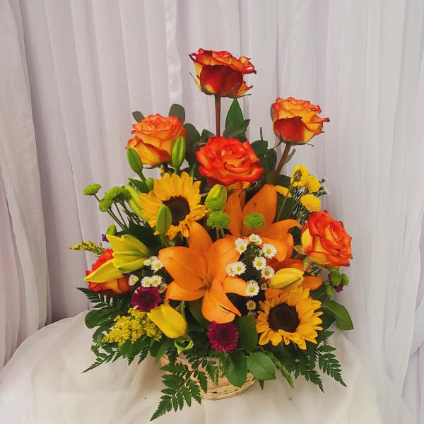 Mixed bouquet of orange roses, lilies, and sunflowers in a basket