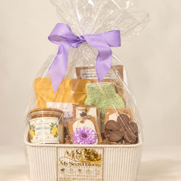 Gift basket wrapped in clear cellophane with a purple bow and assorted items inside