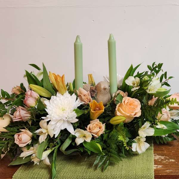 Low floral centerpiece with roses, lilies, and two green candles