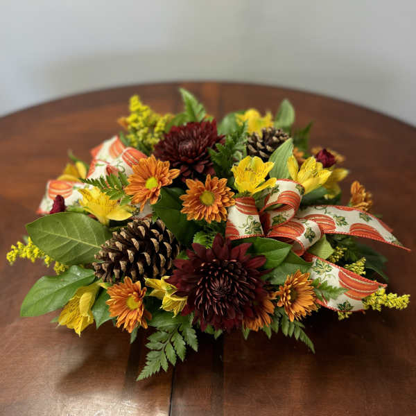 Autumn floral centerpiece with mums, pinecones, and ribbon on a table