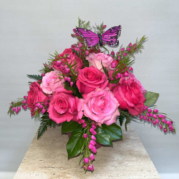 Pink roses with a purple butterfly accent in a vase arrangement