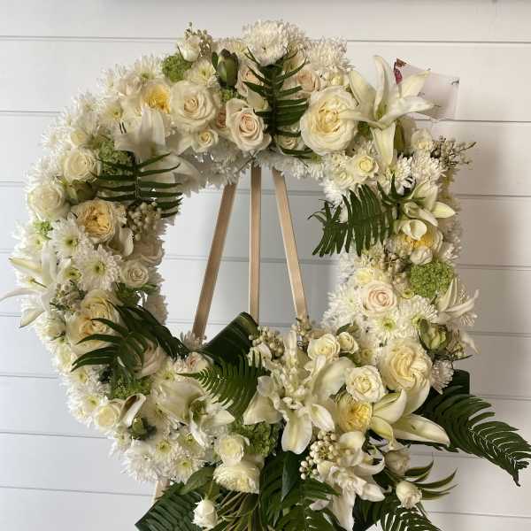 White floral wreath on a wooden easel with roses and lilies