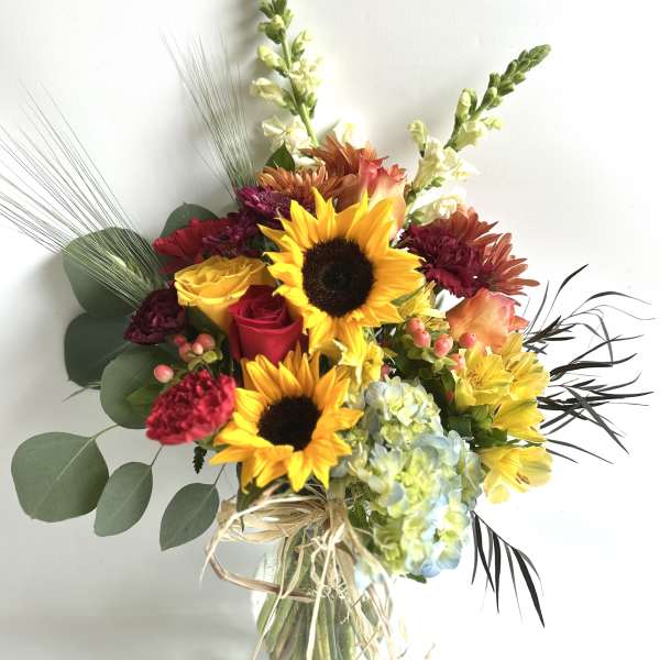 Bouquet of sunflowers, roses, hydrangea, and mixed blooms in a glass vase