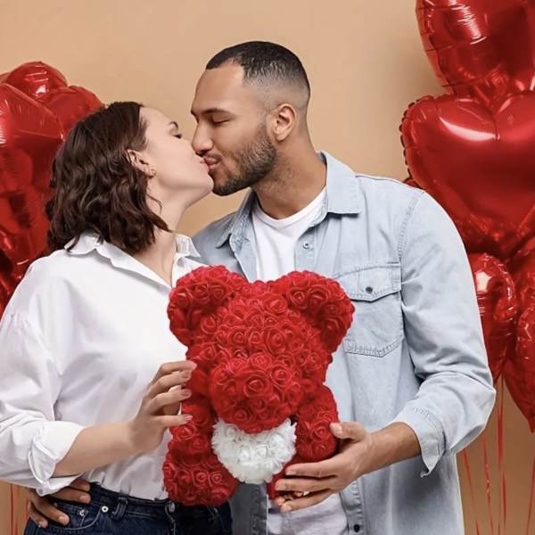 Couple kissing while holding a red rose teddy bear with heart balloons behind them