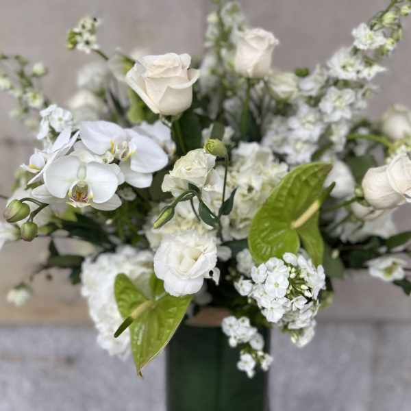White floral arrangement with roses and orchids in a tall vase