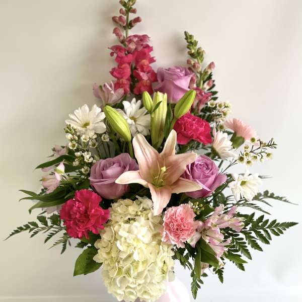 Pink and white mixed flower arrangement in a pale vase