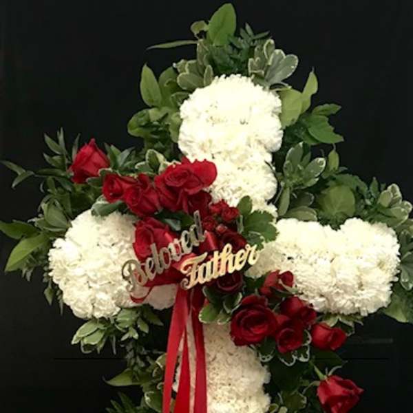 Cross-shaped floral tribute with white blooms and red roses on a black stand