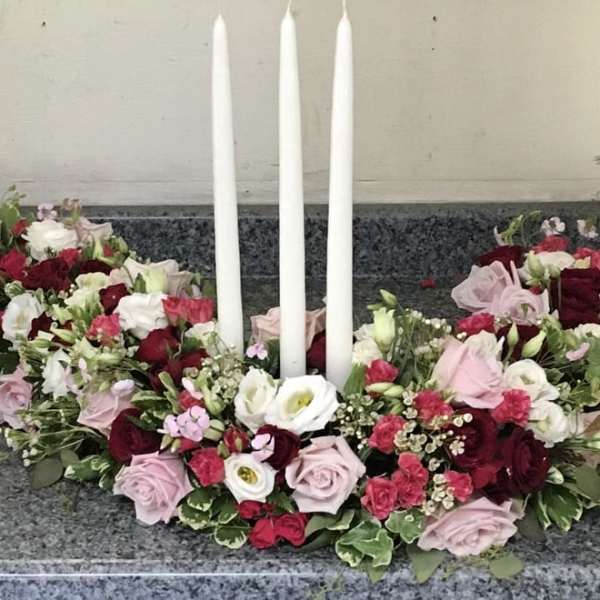 Floral wreath with red, pink, and white roses around three white candles