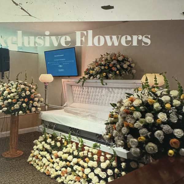 White and peach rose casket spray with matching floral pieces around a white casket