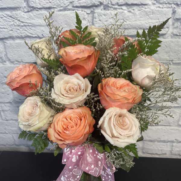 Peach and white roses in a glass vase with a pink ribbon