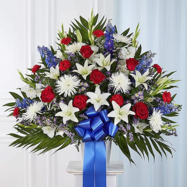 Large standing floral spray with red roses, white lilies, and blue flowers