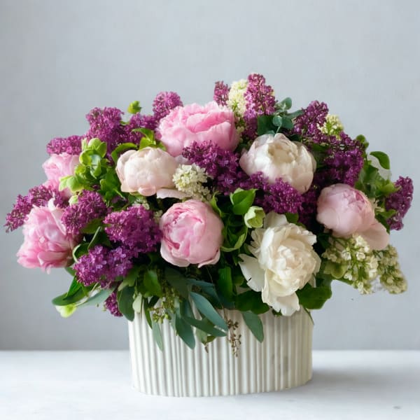 Pink and white peonies with purple lilac in a ribbed cream vase