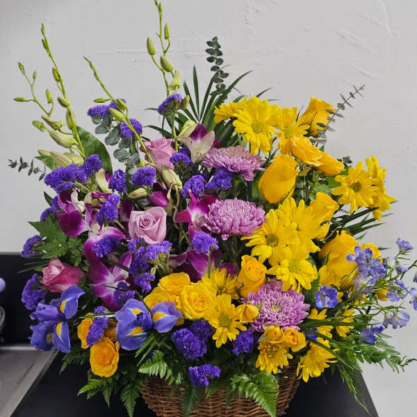 Basket arrangement of yellow daisies, purple orchids, and pink roses