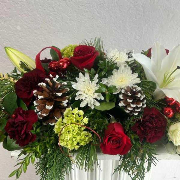 Holiday floral arrangement with red roses, white lilies, and pinecones