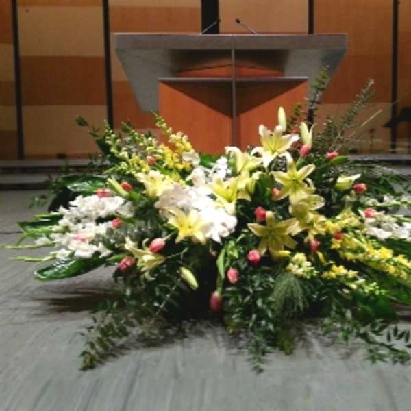 Large altar-style arrangement of yellow lilies, white flowers, and pink buds in front of a podium