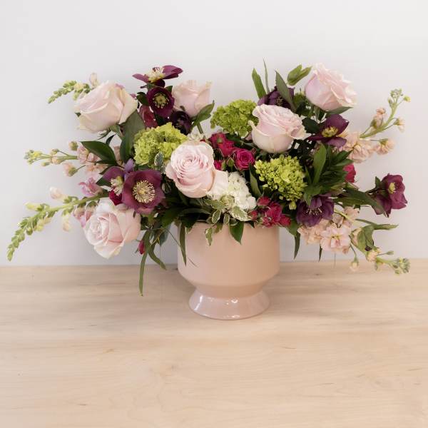 Pink and purple flower arrangement in a blush pedestal vase