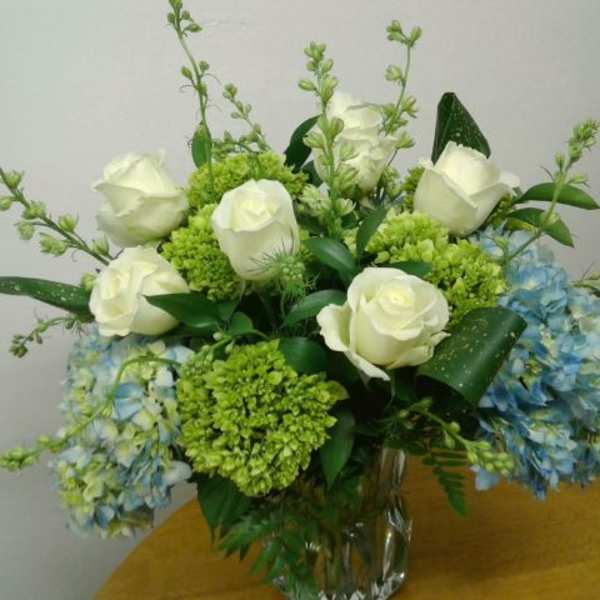 White roses and blue hydrangeas in a clear glass vase
