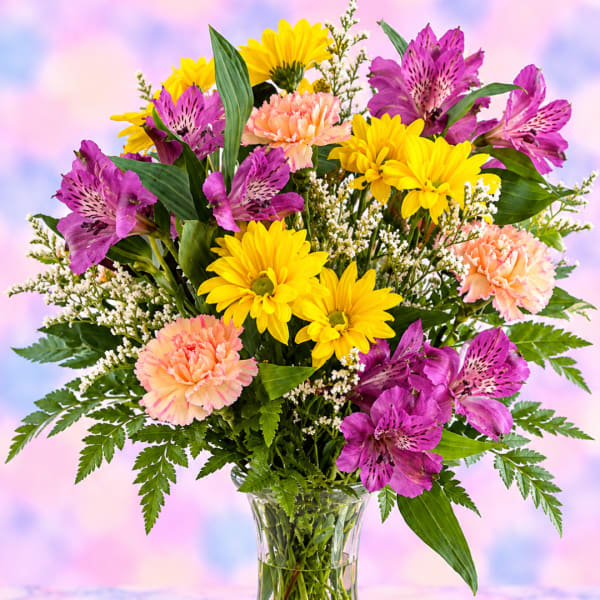 Bouquet of yellow daisies, purple alstroemeria, and peach carnations in a glass vase
