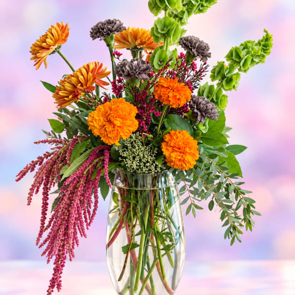 Tall mixed bouquet with orange and gray flowers in a clear glass vase