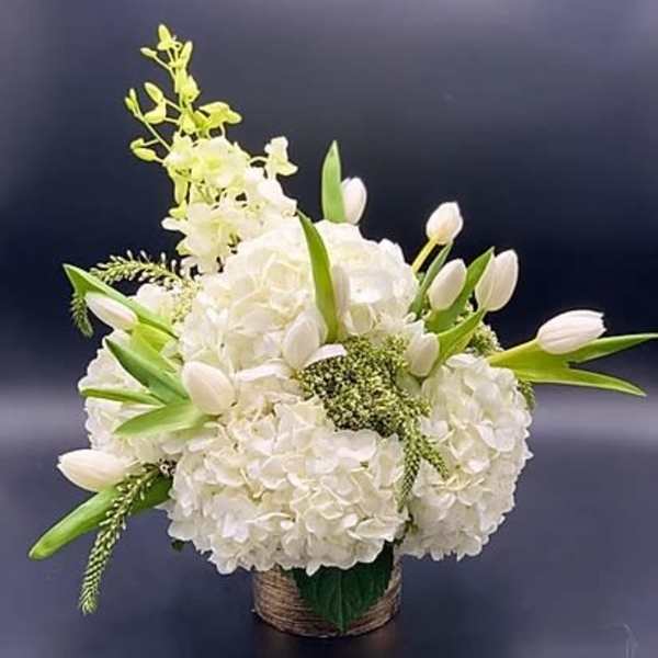 White floral arrangement with tulips and hydrangeas in a woven basket