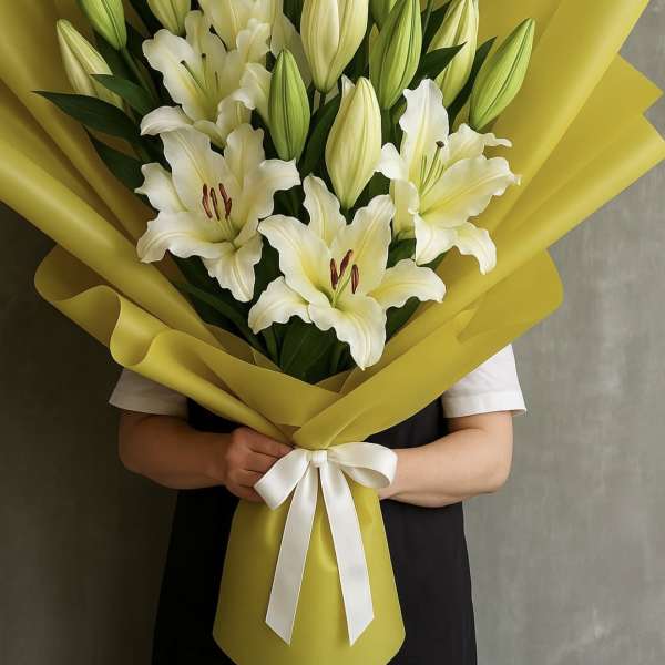 Bouquet of white lilies wrapped in bright yellow paper with a white ribbon