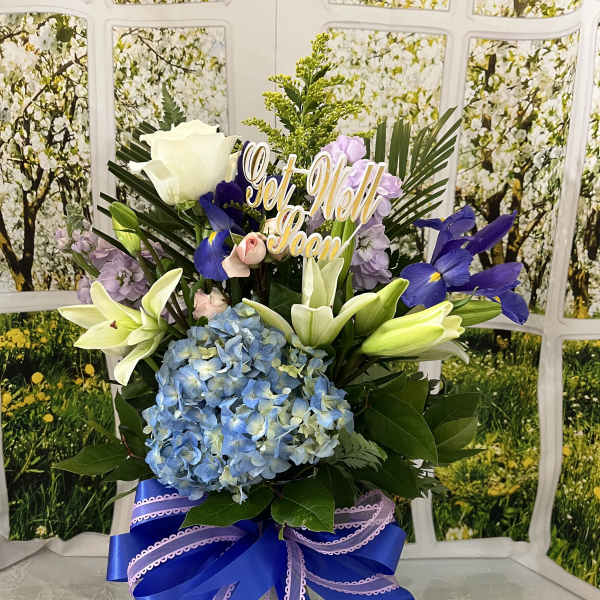 Tall floral arrangement with lilies, hydrangea, and a "Get Well Soon" sign