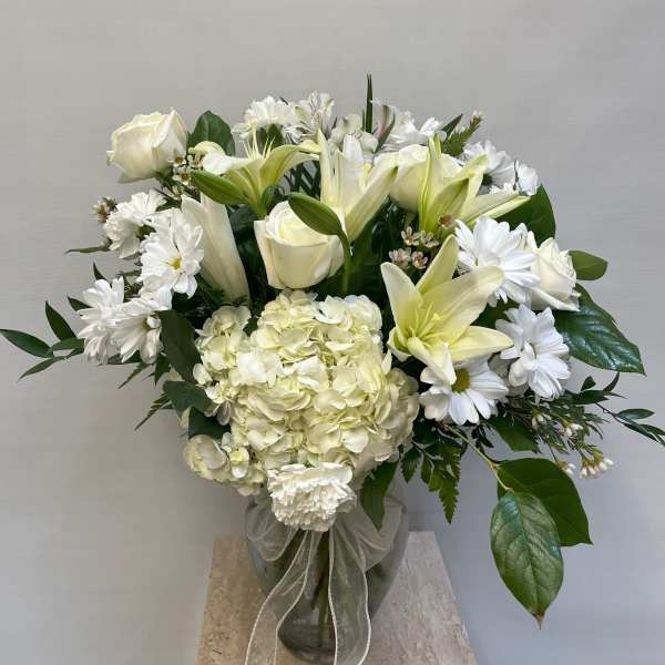 White roses, lilies, and daisies arranged in a glass vase with a ribbon.