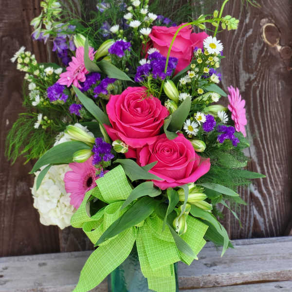 Pink roses and mixed flowers in a glass vase with a green ribbon