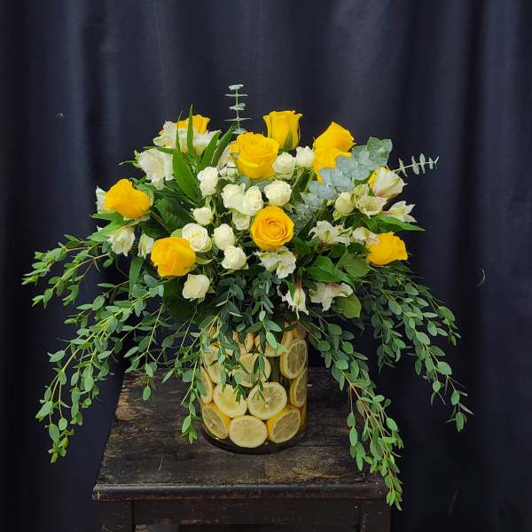 Yellow roses and white spray roses in a lemon-filled glass vase