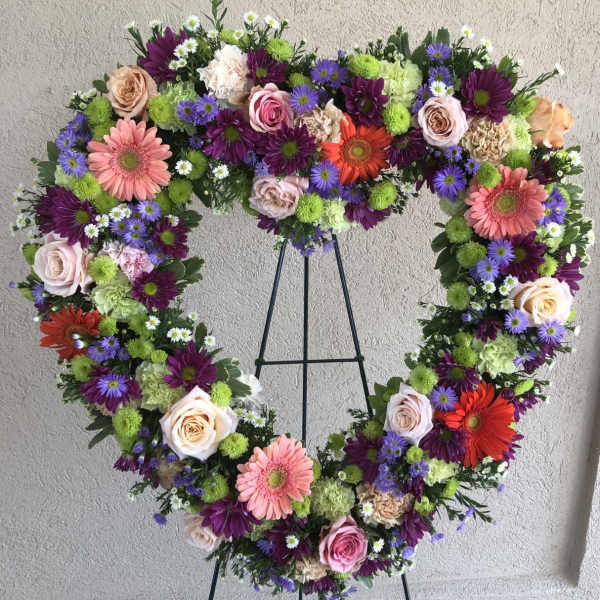 Heart-shaped floral wreath on a black stand with pink, purple, white, and orange flowers