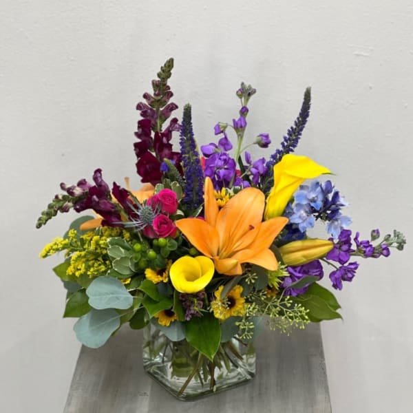 Colorful mixed bouquet in a clear glass vase with lilies, calla lilies, and snapdragons