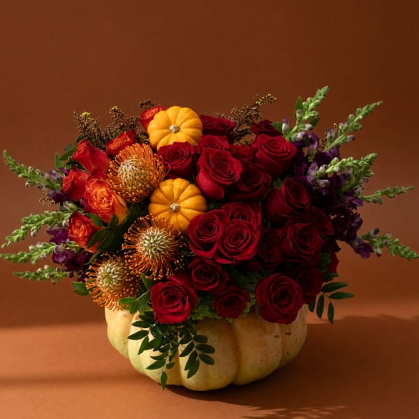 Bouquet of red roses and orange flowers arranged in a pumpkin container