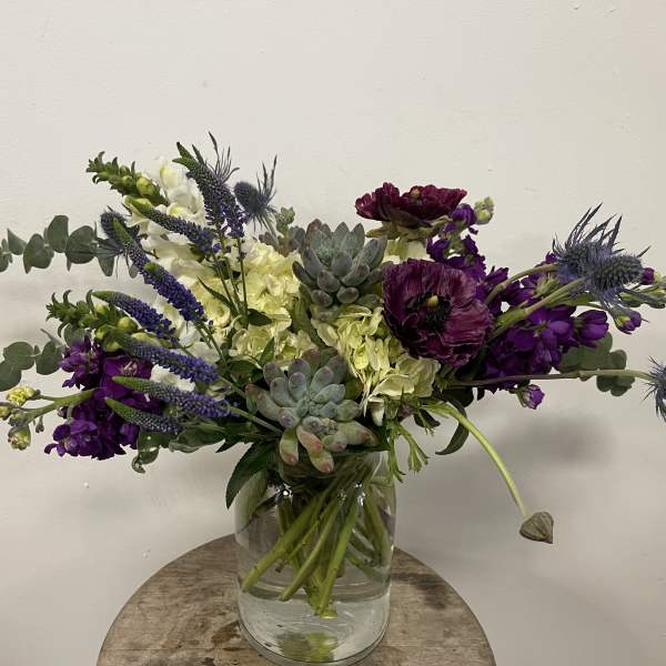 Purple and white floral arrangement in a clear glass vase with succulents