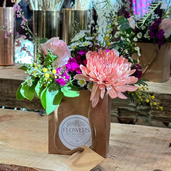 Mixed bouquet in a brown paper gift bag with pink blooms and daisies