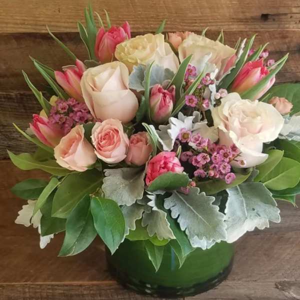 Low arrangement of pink and cream roses and tulips in a green vase with small pink filler blooms
