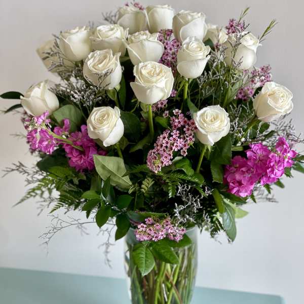 White roses and pink filler flowers arranged in a clear glass vase