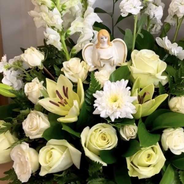 White roses and lilies arranged with tall white snapdragons and a small angel figurine